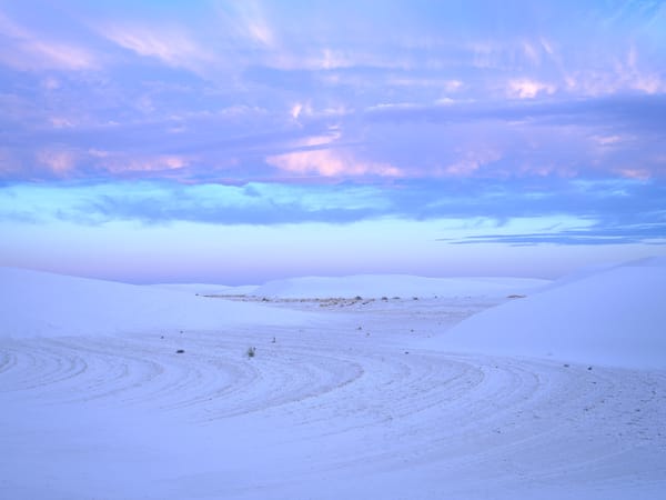 Soft pastel clouds over white sand dunes at sunset in White Sands National Park, with subtle sand patterns in the foreground.