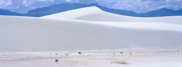 White sand dune with gentle ripples at White Sands National Park, backed by distant mountains under a partly cloudy sky.